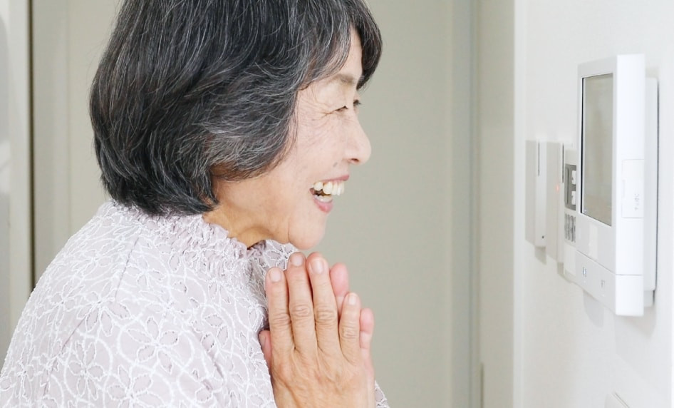 高齢者が室内の温度調整パネルを操作している生活風景