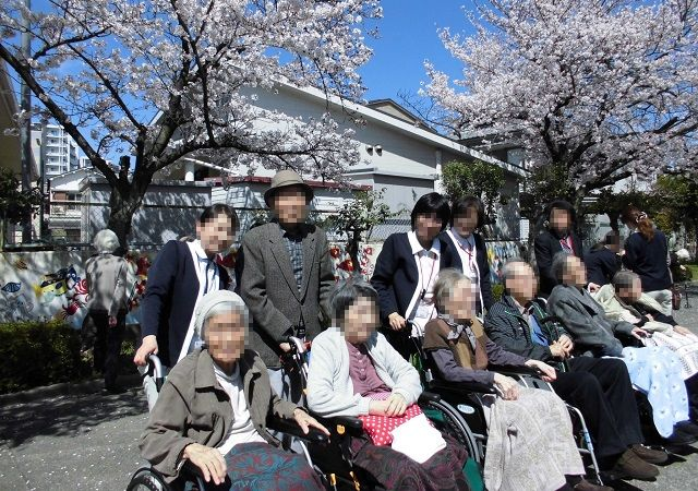 桜の下で入居者と職員が集合写真を撮影している春の行事風景